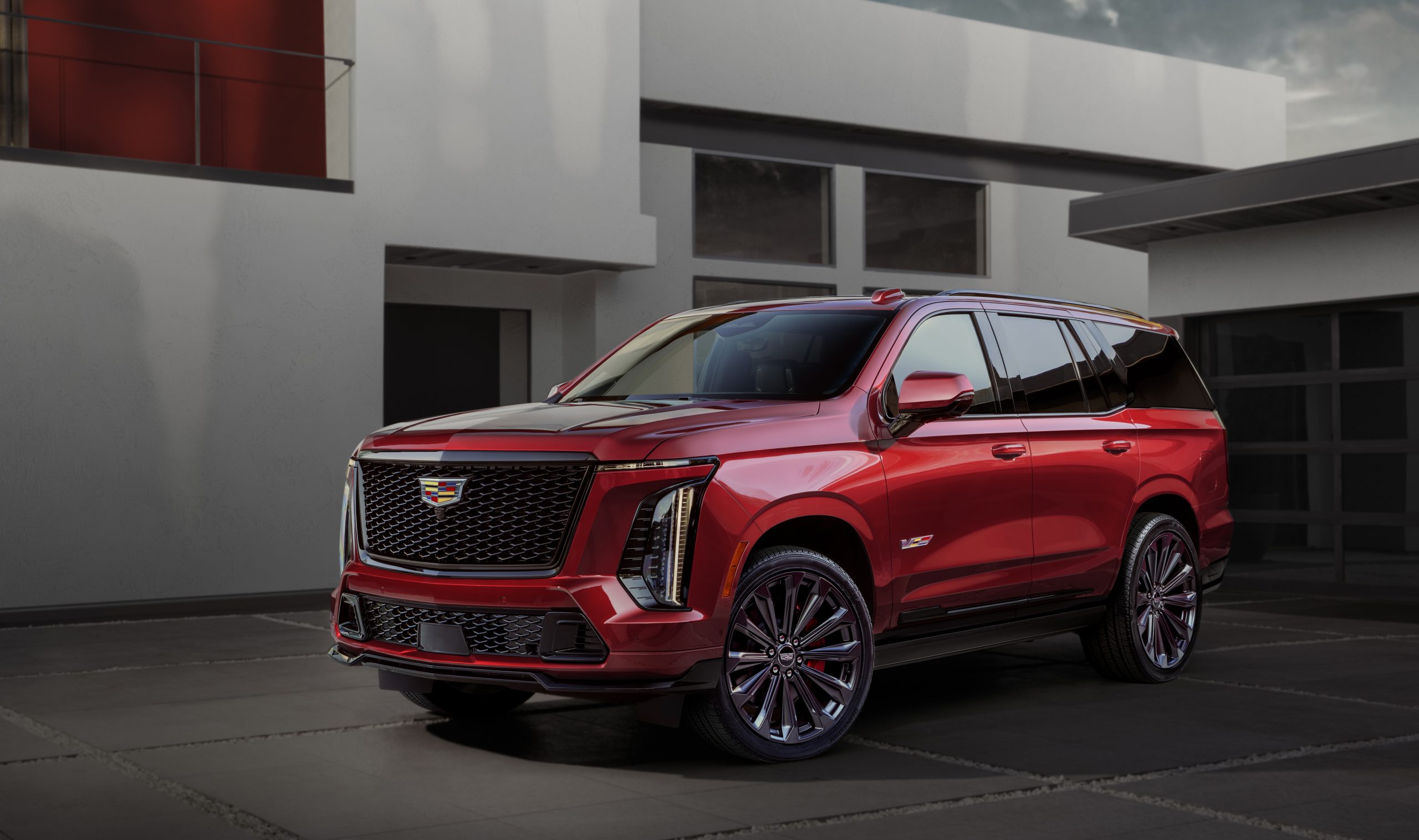 2025 Cadillac Escalade at the top of a mountain with competing SUVs below, showcasing its dominance in the luxury third-row SUV market.