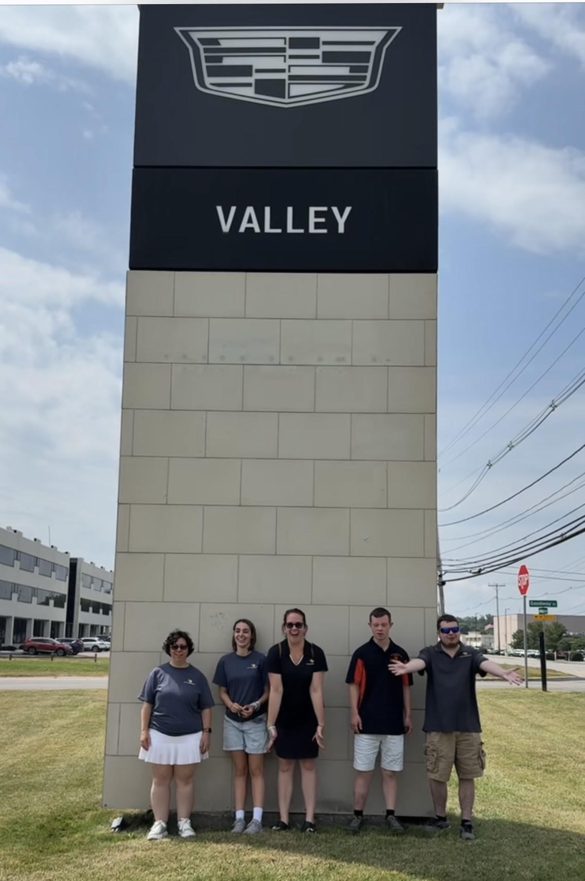 Artists Unlimited cast members standing in front of the Valley Cadillac sign in Rochester, NY, celebrating community partnership and local arts support.
